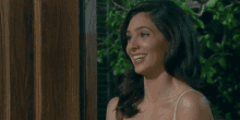 a woman in a white tank top smiles while standing in front of a door
