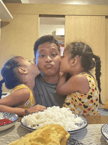 two little girls kissing a man in front of a plate of food