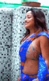 a woman in a blue saree and bikini top is standing in front of a mosaic wall .