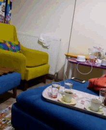 a living room with a yellow chair and a blue ottoman with a tray of cups and saucers on it