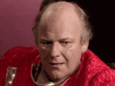a bald man wearing a red jacket and a helmet is making a funny face .