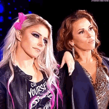 two women are standing next to each other in a dark room . one of the women is wearing a pink headband .