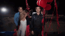 a group of people are standing around red balloons