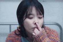 a woman in a colorful sweater is covering her nose with her finger
