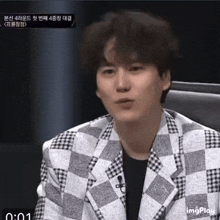 a man wearing a plaid jacket is sitting in front of a microphone with the time 0:00