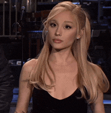 a blonde woman wearing a black dress looks at the camera