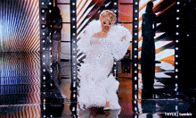 a woman in a white feathered gown is dancing on a stage with t4yce tumblr in the corner
