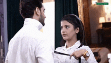 a man and a woman are standing next to each other in a room and the woman is tying the man 's tie .