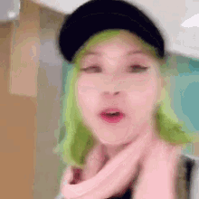 a woman with green hair and a pink scarf is wearing a black hat and a pink scarf .