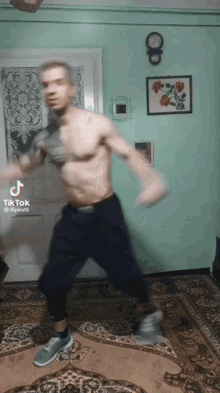 a shirtless man is dancing in a living room with a clock on the wall behind him .