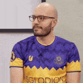 a bald man wearing glasses and a purple and yellow sglodion jersey