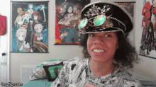 a man wearing a hat and goggles is smiling in front of anime posters on the wall