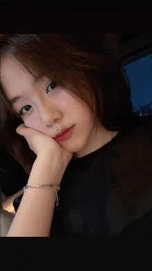 a woman wearing a black shirt and a silver bracelet rests her head on her hand