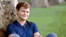 a man in a blue shirt is leaning against a tree with #agt written on the bottom
