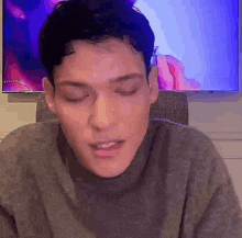 a man is sitting in front of a television with his eyes closed and a sweater on .