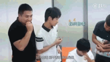 a group of young men are standing in a room with chinese writing on the wall behind them .