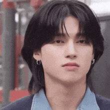 a close up of a young man with long black hair wearing earrings and a denim shirt .