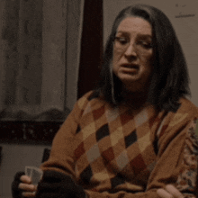 a woman wearing glasses and a plaid sweater holds a cup