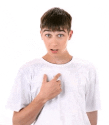 a young boy in a white t-shirt is pointing at his chest .