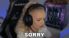 a woman wearing headphones is saying sorry while sitting in front of a mini refrigerator .