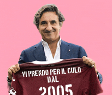 a man in a suit holds a shirt that says vi prendo per il culo dal 2005