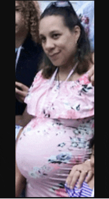 a pregnant woman in a pink floral dress stands in a crowd
