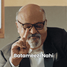 a bald man with glasses and a beard is pointing at his nose with the caption batameezi nahi