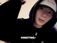 a person wearing a hoodie and a hat with the word waiting written on it .