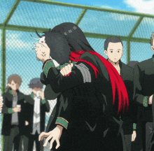 a group of people are standing in front of a chain link fence and one of them has a red scarf around her neck