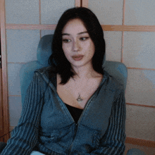 a woman is sitting in a chair wearing a striped jacket and a necklace