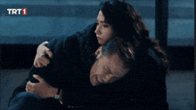 a woman is hugging a man in front of a sign that says trt 1