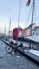 a bicycle is parked next to a red phone booth on a cobblestone street