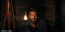 a man with a beard is holding a lantern in a dark room with pranay varma written on the bottom right