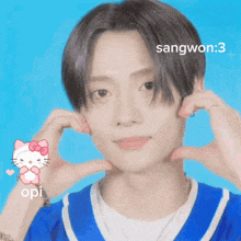 a young man in a blue shirt making a heart shape with his hands with a hello kitty icon behind him