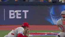 a baseball player catches a ball in front of a bet banner