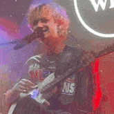 a man singing into a microphone while playing a guitar and wearing a shirt that says nlcs on it