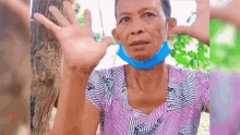 an elderly woman wearing a blue face mask is sitting in front of a tree .