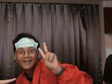 a man wearing glasses and a bandage on his forehead giving a peace sign
