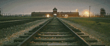 train tracks leading to a building with a tower in the distance