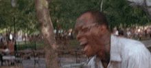 a man with glasses is laughing in a park with trees in the background