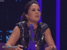 a woman in a sequined top is smiling in front of a microphone with the username lialmeida05