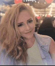 a woman with long blonde hair is smiling and wearing a blue denim vest .