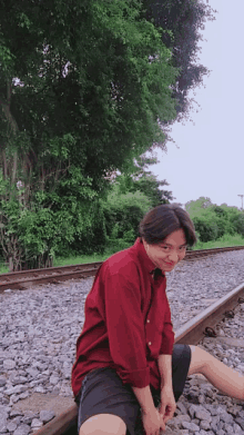 a man in a red shirt is sitting on the train tracks