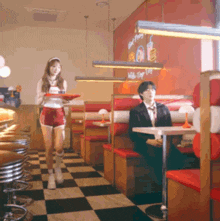 a man sits at a table in a diner while a woman carrying a tray walks past him