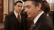 a man in a suit and tie stands next to another man in a suit