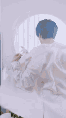 a man with blue hair is standing in front of a mirror in a room .