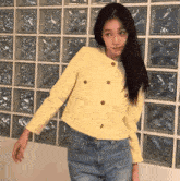 a woman wearing a yellow jacket and blue jeans is standing in front of a glass wall