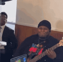 a man is playing a guitar in front of a laptop computer