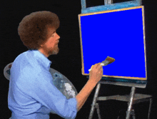 a man is painting a blue screen with a brush on an easel