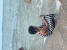 a boy in a striped shirt is laying on the beach near the water